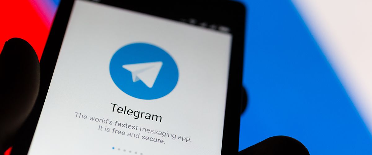 EIn Smartphone mit der geöffneten App Telegram, im Hintergrund eine russische Flagge